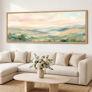 May include: A panoramic landscape painting in a light wooden frame featuring rolling hills in shades of sage green, soft peach, and cream. The artwork displays visible brushstrokes depicting a hazy horizon under a pale, warm-toned sky.