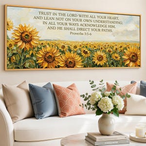 May include: A framed canvas art piece featuring a field of sunflowers in a textured, impressionistic style. The artwork includes the text "TRUST IN THE LORD WITH ALL YOUR HEART... Proverbs 3:5-6". The painting is displayed above a white sofa with decorative pillows.