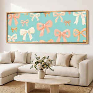 Puede incluir: Una pieza de arte mural rectangular con un patrón repetitivo de lazos color melocotón, crema y naranja claro sobre un fondo azul verdoso claro sólido. La obra está enmarcada en un marco de madera clara y delgada y dispuesta horizontalmente.