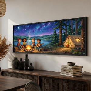 May include: A panoramic framed wall art print depicting a nighttime camping scene with four children sitting around a campfire by a lake. One child plays a guitar while others roast marshmallows. A lit tent stands nearby under a starry night sky.