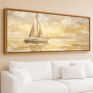 May include: A framed canvas art print depicts a sailboat on calm water under a cloudy sky. The artwork features a palette of beige, cream, and gold tones, creating a serene and warm atmosphere. The rectangular frame is made of wood.