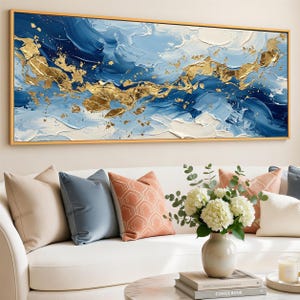 May include: Abstract art painting with a gold frame. The artwork features a textured design with shades of blue, white, and gold. The painting is displayed above a white sofa with decorative pillows and a vase of flowers.