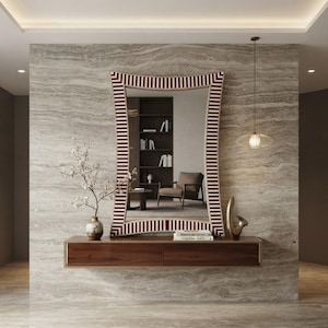 May include: A rectangular wall mirror with a curved frame featuring a repeating pattern of thin dark brown and white stripes. The mirror is mounted above a dark wood floating console table with two drawers, holding a vase and a decorative object.