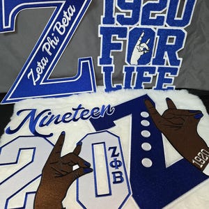 May include: Blue and white embroidered patches with the text "Zeta Phi Beta", "1920 FOR LIFE", and "Nineteen 20". The patches feature hand gestures and the letters "ZΦB".
