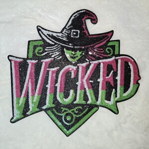 May include: A sequined patch featuring the word "WICKED" in pink, green, and white, with a witch's hat and face above. The design is set against a black background with green accents, perfect for Halloween or witch-themed crafts.