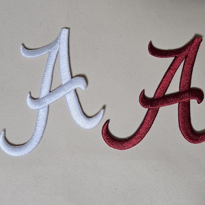 May include: Two embroidered letter "A" patches. One is white, the other is maroon. The script-style letters are stitched with a satin finish. These patches are suitable for apparel, bags, or other fabric items.