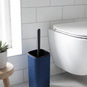 Peut inclure: Un ensemble brosse de toilette bleu foncé comprenant un support carré à texture nervurée verticale et un intérieur noir. Le manche noir assorti se tient droit dans le support, conçu avec des coins arrondis et une base solide.