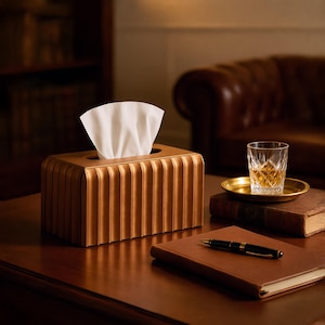 May include: A rectangular tissue box cover with a metallic bronze finish and vertical fluted ridges. The box features a central rectangular opening at the top, from which a single white paper tissue is partially pulled out and standing upright.