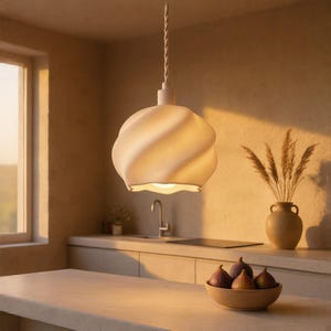 May include: A matte white pendant light with a spiraled, twisted shape hangs from a matching twisted cord. The light fixture features a soft, rounded silhouette with a wide opening at the bottom, emitting a warm glow in a kitchen setting.