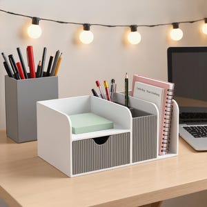 Könnte beinhalten: Ein weißer Schreibtisch-Organizer mit einer grauen, gerippten Schublade und einem passenden grauen Stiftehalter. Der Organizer enthält einen Stapel hellgrüner Haftnotizen, mehrere Stifte und ein Spiralnotizbuch mit Text auf dem Einband.