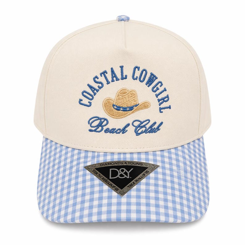 May include: Cream-colored baseball cap with a blue and white gingham brim. The cap features the embroidered text "COASTAL COWGIRL Beach Club" above a cowboy hat graphic. A small tag at the bottom reads "DIAMONDS & YOUNG".