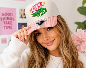 Gorra Later Gator Trucker: Cocodrilo bordado, visera con franja rosa, cierre ajustable.