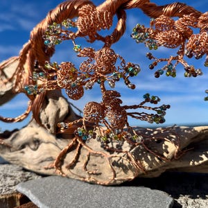 Peut inclure: Sculpture d'arbre en fil de cuivre avec des branches complexes et des accents de perles vertes, bleues et ambrées. L'arbre est monté sur un morceau de bois flotté, sur fond de ciel bleu et d'océan.