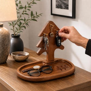 May include: A dark brown wooden organizer featuring a tree-shaped stand with gold hooks for keys and an oval tray base. The tray is engraved with the name WILLIAM and a monogram. A wristwatch and black-rimmed glasses rest on the tray surface.