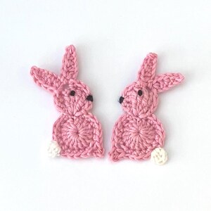 May include: Two handmade pink crochet bunny appliques with black eyes and white cotton tails. These Easter-themed decorations are perfect for crafting projects, adding a touch of whimsy to clothing, accessories, or home decor. The bunnies are approximately 5 cm tall.