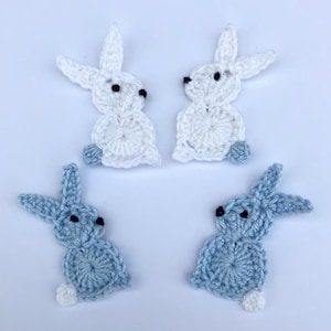May include: Four crocheted bunny rabbit shapes, two white and two light blue. The bunnies are all facing forward with their ears up.