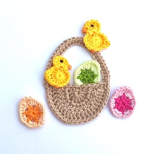 May include: A crocheted Easter basket with two yellow chicks, a green and white egg, and two decorative eggs in shades of pink and orange. The basket and eggs are set against a white background.