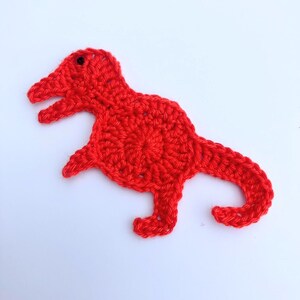 May include: A red crocheted dinosaur toy. The dinosaur has a small black eye and is made with a single crochet stitch.