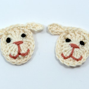 May include: Two crocheted lamb faces. Each lamb face is cream-colored with black eyes and a pink mouth. The ears are also cream-colored and extend from the top of the head. These would be great for a baby shower or Easter.