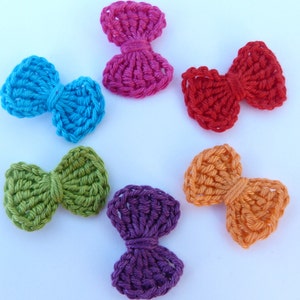May include: Six crocheted bows in different colors: teal, pink, red, green, orange, and purple. The bows are arranged in a circle on a white background.