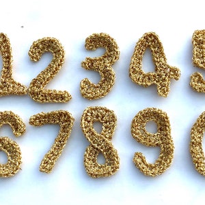 Könnte beinhalten: Zehn goldene Häkelzahlen von 1 bis 10 auf weißem Hintergrund.