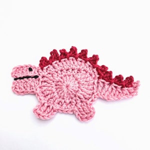 May include: A pink crocheted dinosaur with a red crocheted spine.