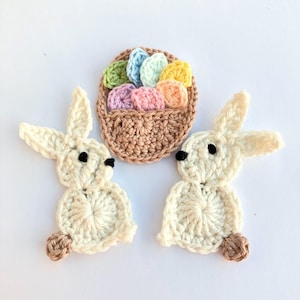 May include: Crocheted Easter-themed set featuring two white bunnies with brown accents and a basket filled with pastel-colored eggs. The basket and bunnies are made of yarn, perfect for spring decor or crafting projects.