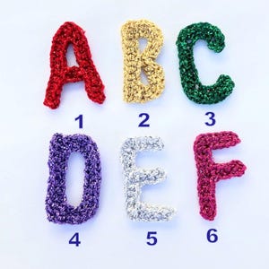 May include: Six crocheted letters, A through F, in different colors and glitter finishes. The letters are numbered 1 through 6.