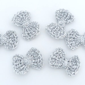 May include: Five silver crocheted bows. The bows are small and delicate, with a slightly textured surface.