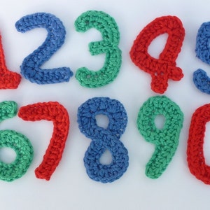 Könnte beinhalten: Gehäkelte Zahlen von 1 bis 10 in Rot, Blau und Grün. Die Zahlen sind aus Garn gefertigt und etwa 5 cm hoch.