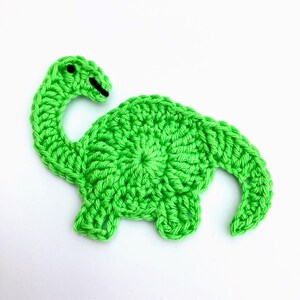 May include: A green crocheted dinosaur applique. The dinosaur has a long neck and a round body.