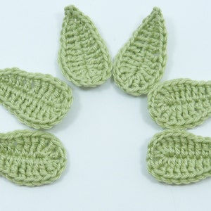 May include: Six crocheted green leaf shapes, arranged in a circle on a white background.