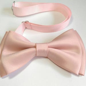 May include: A light pink bow tie with an adjustable strap. The bow tie is made of satin and has a classic shape.