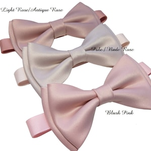 May include: Three satin bow ties in different shades of pink. The top bow tie is light rose, the middle bow tie is pale nude rose, and the bottom bow tie is blush pink.