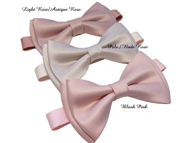 May include: Three satin bow ties in different shades of pink. The top bow tie is light rose, the middle bow tie is pale nude rose, and the bottom bow tie is blush pink.