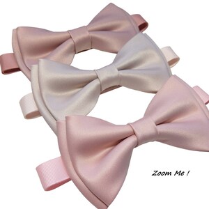 May include: Three satin bow ties in shades of pink and beige. The bow ties are arranged in a stack, with the lightest shade on top and the darkest shade on the bottom. The bow ties are tied with a ribbon and have a "Zoom Me!" label.