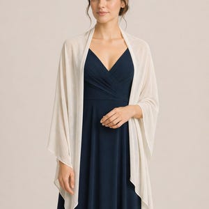 May include: A cream-coloured shawl draped over a navy blue dress. The shawl has a soft, flowing appearance, with a simple, elegant design. The dress features a V-neckline. The overall look is sophisticated and suitable for formal occasions.