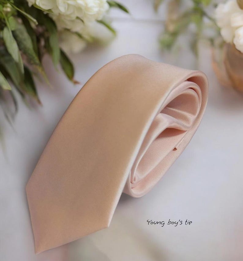 May include: A light pink satin tie. The tie is folded in half and the ends are tucked inside the fold. The text "Young boy's tie" is written in the bottom right corner of the image.