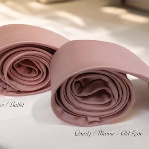 May include: Two rolled neckties in shades of pink, one labelled "Light Rose / Ballet" and the other "Quartz / Mauve / Old Rose." The ties are made of a smooth fabric and are displayed on a white surface.
