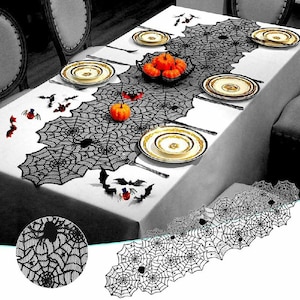 May include: A black lace table runner featuring a repeating spider web pattern with integrated spider motifs. The runner is displayed on a white tablecloth set with plates, small orange pumpkins, and scattered bat-shaped decorations.