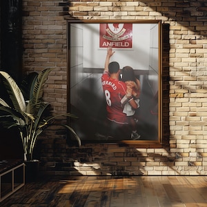 May include: A framed photograph featuring a red Liverpool Football Club jersey with the name "Gerrard" and the number 8. The photo shows a person in the jersey with their arm raised, standing in front of the Anfield sign. The image is displayed on a brick wall.