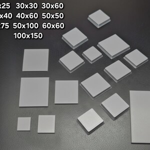 Könnte beinhalten: Eine Ansammlung grauer, quadratischer und rechteckiger Fliesen in verschiedenen Größen, darunter 25x25mm, 30x30mm, 30x60mm, 40x40mm, 40x60mm, 50x50mm, 50x75mm, 50x100mm, 60x60mm und 100x150mm. Die Fliesen liegen auf einer dunklen Oberfläche.