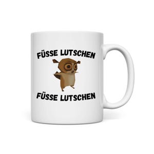 May include: White ceramic mug featuring a cartoon lemur character. The mug has the text "FÜSSE LUTSCHEN" in black, above and below the lemur illustration. The lemur is brown and tan with large eyes.