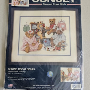 May include: A Sunset Stamped Cross Stitch kit titled Sewing Room Bears, designed by Janet Kruskamp. The packaging features an illustration of teddy bears in a sewing room, measuring 14 inches by 11 inches, with fabric size 18 by 15 inches.