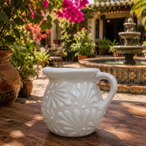 May include: A white ceramic pitcher featuring a rounded body and a single handle. The exterior surface is decorated with a raised, embossed floral pattern consisting of repeating petal-like shapes and small dots covering the entire rounded base.