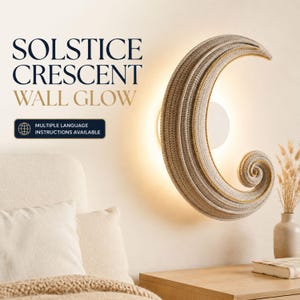 Könnte beinhalten: Eine halbmondförmige Wandleuchte mit beiger Häkelstruktur und goldener Verzierung. Der Text SOLSTICE CRESCENT WALL GLOW sowie ein rechteckiges Etikett mit der Aufschrift MULTIPLE LANGUAGE INSTRUCTIONS AVAILABLE sind neben der leuchtenden Lampe zu sehen.