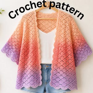 Pode incluir: Um cardigan com padrão de crochê em um gradiente de cores, do pêssego ao vermelho e ao roxo. O cardigan aberto tem uma borda ondulada e é exibido em um cabide de madeira. As palavras "Crochet pattern" estão escritas em preto acima do cardigan.