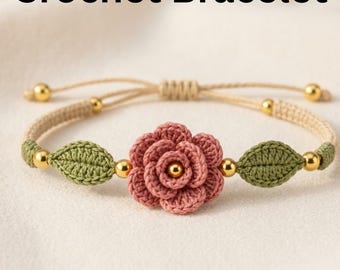 Pode incluir: Uma pulseira de crochê com uma rosa rosa e folhas verdes. A pulseira tem um cordão bege com contas douradas. O texto "Crochet Bracelet" está na parte superior da imagem.