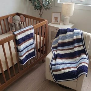 May include: A wooden crib with a crocheted blue, brown, and white striped blanket draped over the side. A matching blanket is draped over a chair. An elephant stuffed animal sits inside the crib.