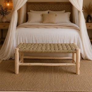 May include: A bedroom scene with a woven bench at the foot of a bed with a woven headboard. The bed has white linens and a beige throw. The room has a neutral colour palette with a woven rug and sheer curtains.